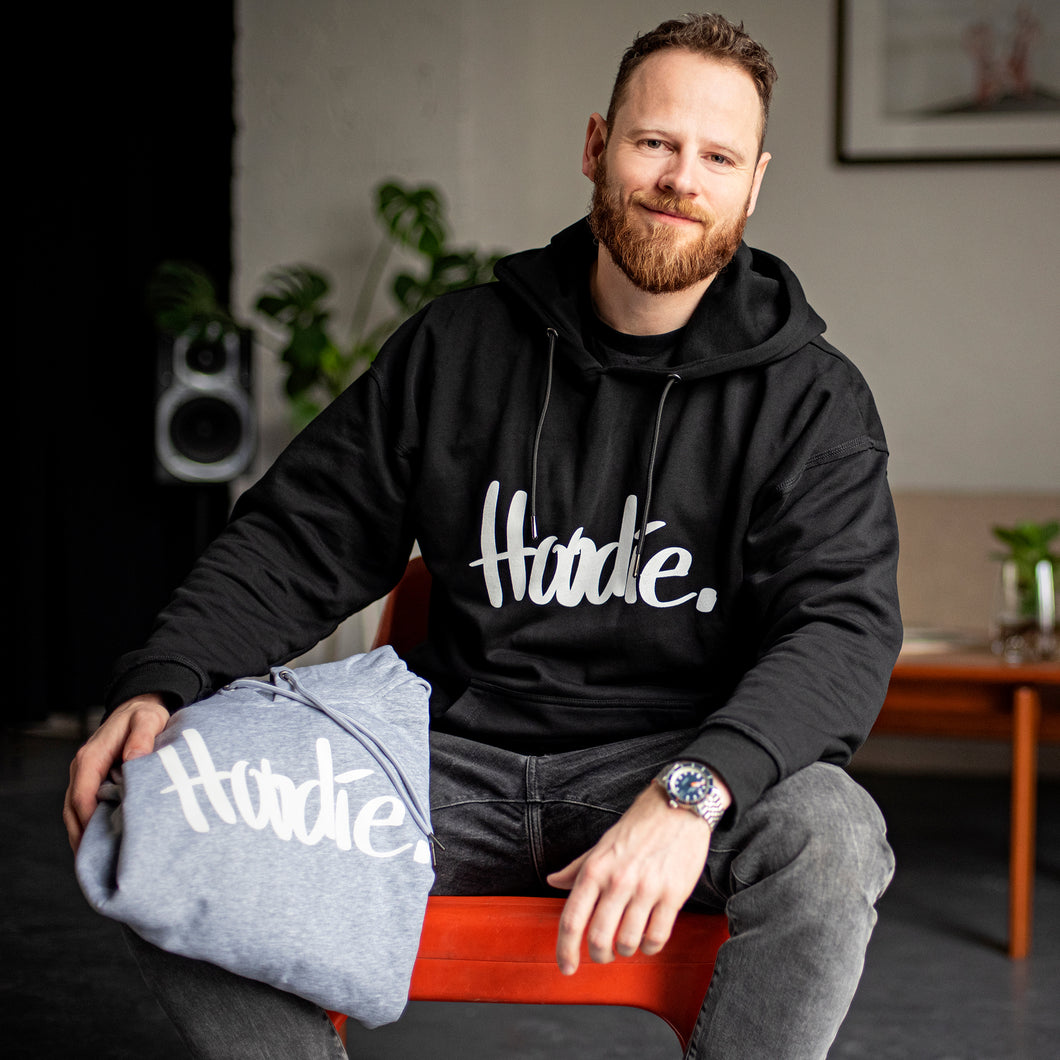 Portraitfoto von Chris Hillus mit neuem Design des Hoodie mit Schriftzug HOODIE. Hoodie in Schwarz und Hellgrau, Oversize und Overgemütlich